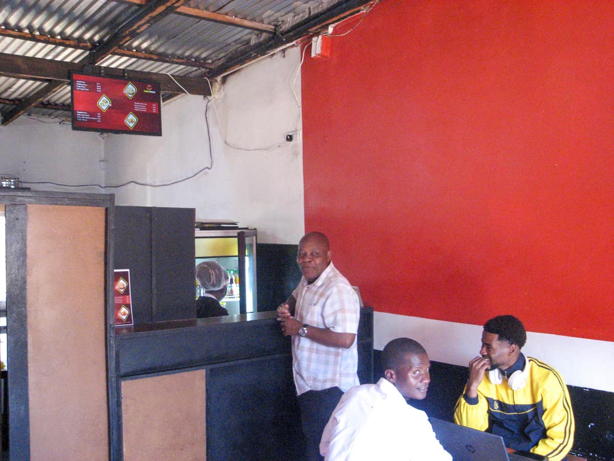 Customers at the counter inside Queso Pizza in Chongwe, under the menu board